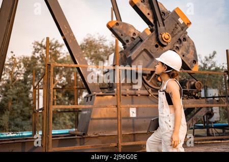 Ingegneria petrolchimica asiatica donna con casco di sicurezza in piedi nella struttura petrolifera industria petrolchimica. Foto Stock