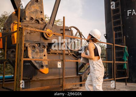 Ingegneria petrolchimica asiatica donna con casco di sicurezza in piedi nella struttura petrolifera industria petrolchimica. Foto Stock