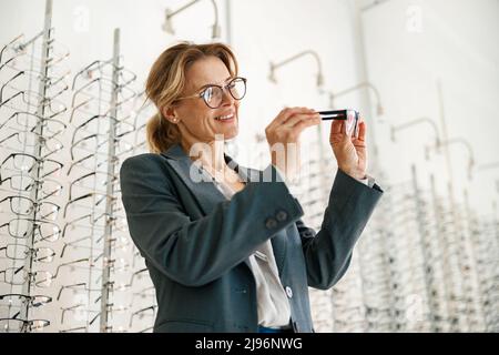 Donna sceglie tra due bicchieri in un negozio di ottico Foto Stock