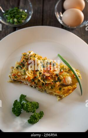 Un pezzo di torta a base di pesce, uova, cipolle e carote. Piatto bianco, tavole di legno Foto Stock