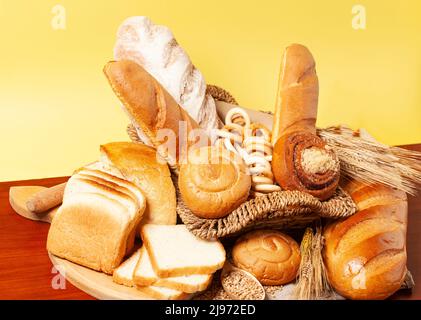 Sfondo culinario con pane, panini, bagel secchi, spighe di grano in un cestino di vimini, vista dall'alto Foto Stock
