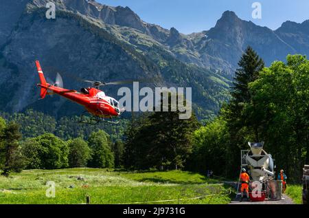 Maienfeld, Svizzera - 20 maggio 2022: Elicottero che si prepara a trasportare un carico di cemento da un camion di cemento a una montagna lontana delle Alpi svizzere Foto Stock