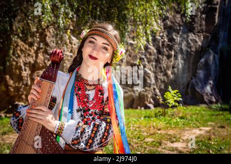 Il musicista ucraino in autentico vestito nazionale siede su una roccia. Donna Ucraina con uno strumento musicale bandura prima di eseguire musica folk Foto Stock