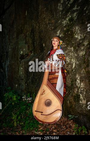 Un musicista ucraino in abiti nazionali si alza con una bandura appoggiata su una roccia. Foto Stock