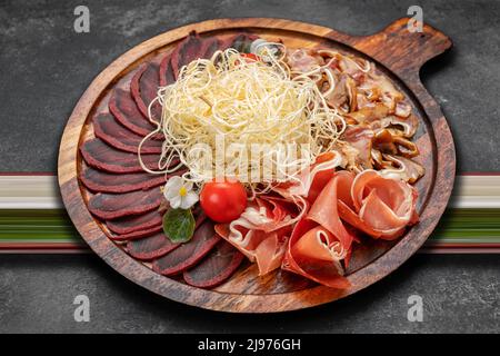 Set di spuntini per birra, calamari secchi, basturma, jamon, orecchie di maiale e pomodori ciliegini, su sfondo scuro Foto Stock