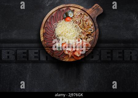 Set di spuntini per birra, calamari secchi, basturma, jamon, orecchie di maiale e pomodori ciliegini, su sfondo scuro Foto Stock