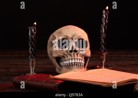 Composizione satanica del cranio umano con libro satanico e candele brucianti. Rituale con bibbia satanica aperta. Foto Stock