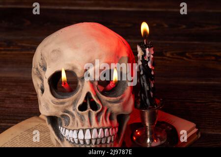 Mockup cranio umano con candele brucianti nei suoi occhi. Sfondo di legno scuro. Foto Stock