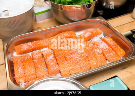 Vassoio di metallo con filetti di salmone crudo sotto sale grosso. Salato prima di cucinare. Foto Stock