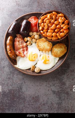 Colazione irlandese con uova fritte, salsicce, budino nero, fagioli al forno, pancetta, pomodoro, crocchette di patate e funghi grigliati in primo piano nel piatto sulla linguetta Foto Stock