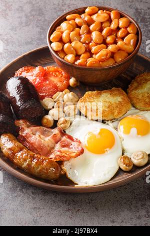 Colazione irlandese con uova fritte, salsicce, budino nero, fagioli al forno, pancetta, pomodoro, crocchette di patate e funghi grigliati in primo piano nel piatto sulla linguetta Foto Stock