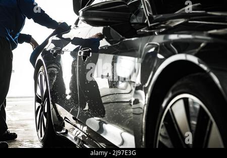 Dettaglio del lavoratore che prepara la carrozzeria dell'auto per la ceratura. Rimozione dell'acqua dagli elementi laterali del veicolo con un panno morbido. Tema industria automobilistica. Foto Stock