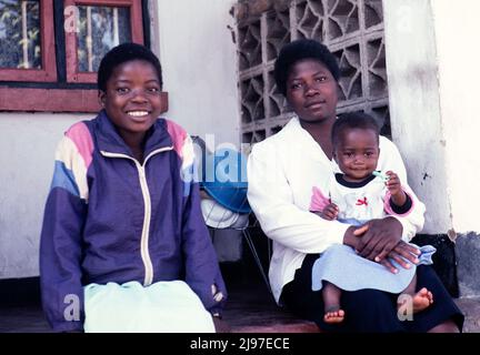 Donna e bambino seduti con adolescente fuori da una casa, Malawi, Africa meridionale, 1995 Foto Stock