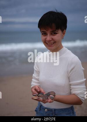 trasgender guardando la fotocamera con un maglione bianco e le conchiglie nelle sue mani Foto Stock