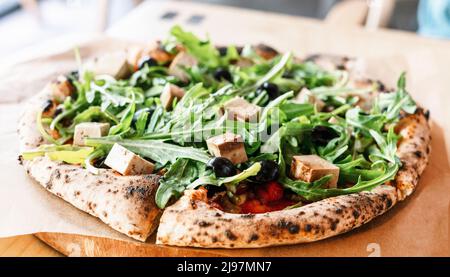 pizza vegana con rucola o rucola tofu olive e pomodori primo piano tavola di legno vegetariano cibo sano mangiare Foto Stock