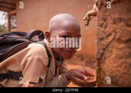 Il bambino nero della scuola raccoglie l'acqua con le mani dal rubinetto situato nel cortile della scuola. Concetto di acqua. Foto Stock