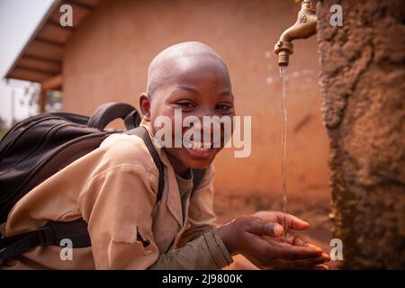 Il ragazzo africano a scuola sorride bevendo acqua dal rubinetto fuori nel cortile. Foto Stock