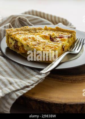 Una fetta placcata di quiche lorraine fatta in casa con una forchetta, posta su un tovagliolo a righe. Foto Stock