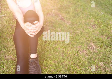 Sezione bassa di sportive che soffrono di dolori articolari seduti sulla via durante la giornata di sole Foto Stock