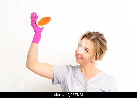 Ritratto di una beautician caucasica femmina che tiene un vaso di pasta di zucchero per zuccherare indossando guanti rosa su sfondo bianco Foto Stock