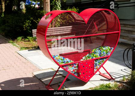 contenitore a forma di cuore rosso per tappi in plastica per bottiglie raccolti per cause benefiche in strada Foto Stock