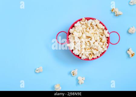 Popcorn arioso in un secchio di ferro rosa su sfondo blu. La vista superiore con spazio di copia. Ora del film. Foto Stock