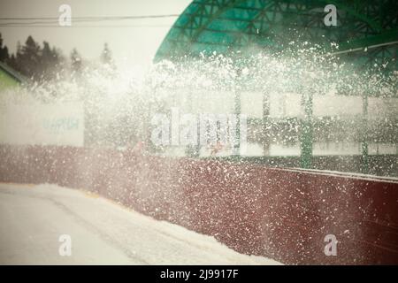 Neve sulla pista di pattinaggio. Sgombero della neve. Piccoli fiocchi di neve volano a bordo. Rimozione dello strato di sedimento dal ghiaccio. Foto Stock