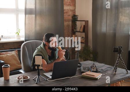Scatto orizzontale di bell'uomo medio-orientale seduto al tavolo di fronte al laptop impostazione microfono per avviare streaming online Foto Stock