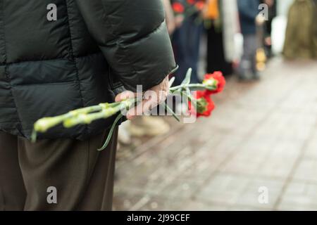 Due garofani in mano all'uomo. Dettagli della cerimonia funebre. Fiori commemorativi in mano. Uomo al funerale. Foto Stock