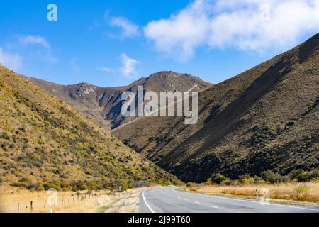 Strada attraverso pieghe di tussock e scopa creste di montagna rivestite Lindis Pass, Canterbury Sud Nuova Zelanda. Foto Stock