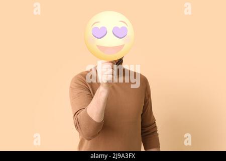 Giovane uomo che tiene felice emoticon con occhi a forma di cuore su sfondo colorato Foto Stock