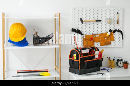 Luogo di lavoro con diversi strumenti moderni e scaffale vicino alla parete luminosa Foto Stock