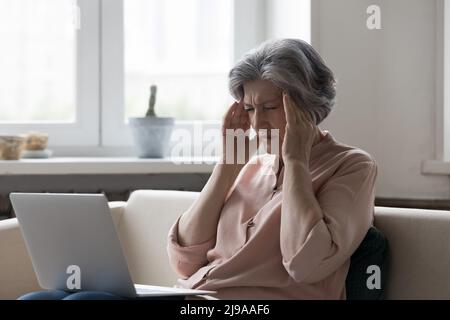 Donna anziana stressata che tocca la testa con gli occhi chiusi Foto Stock