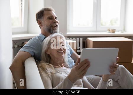 Coppia sposata matura e allegra che si rilassa sul divano dopo le attività di trasferimento Foto Stock