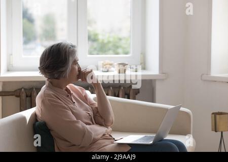 Pensieroso frustrata matura 60s donna che tiene un computer portatile Foto Stock