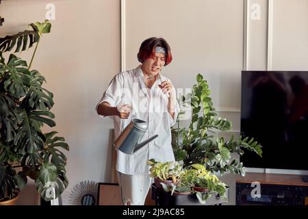 Elegante ragazzo che ascolta musica con cuffie e innaffiare vasi di fiori Foto Stock