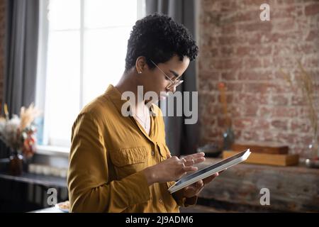 Donna africana seria e focalizzata che lavora con tablet digitale Foto Stock