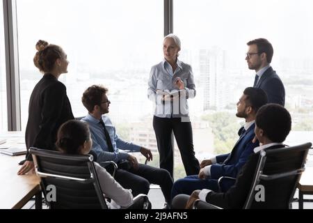 Il vecchio capo dell'azienda conduce il briefing con il personale giovane in ufficio Foto Stock