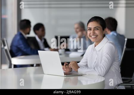 Una donna d'affari indiana si siede alla scrivania con un computer portatile guardando la macchina fotografica Foto Stock