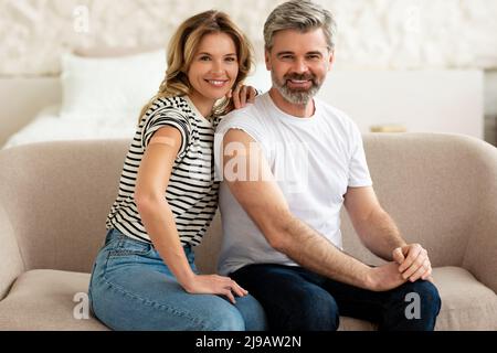 Marito e moglie vaccinati che mostrano armi con Plaster a casa Foto Stock