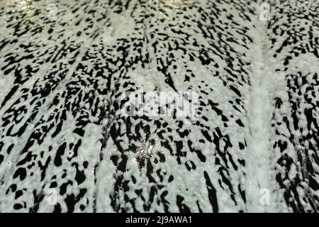 Schiuma di sapone su auto. Texture di schiuma bianca su auto nera. Lavaggio del trasporto. Detersivo sulla superficie. Foto Stock