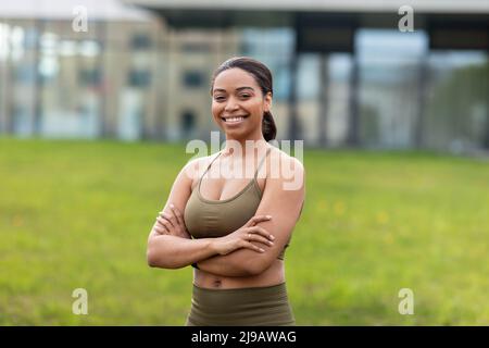 Ritratto di felice giovane donna nera in vestito sportivo in posa al parco urbano Foto Stock