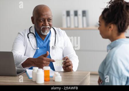 Maturo esperto medico nero che mostra pillole a donna incinta Foto Stock