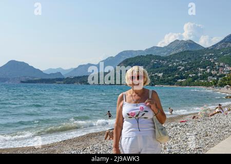 Donna bionda sorridente mature plump si trova sullo sfondo della spiaggia nella città di Bar, Montenegro. Foto Stock