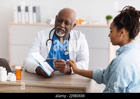Medico maturo nero che spiega il piano di trattamento alla paziente femminile Foto Stock