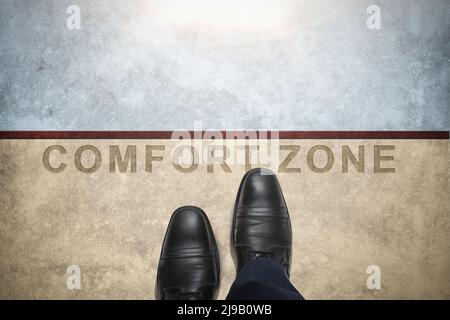 Concetto di zona di comfort, maschio con scarpe in pelle passi sopra una parola con linea su pavimento in cemento, vista dall'alto. Uscite dalla vostra zona comfort e accedete a Oppo Foto Stock