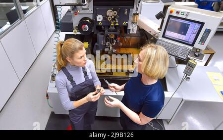 Una tirocinante femminile riceve lezioni tecniche dal suo istruttore. Entrambe le donne lavorano come ingegneri computerizzati di controllo numerico. Foto Stock