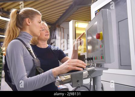 Una tirocinante femminile riceve lezioni tecniche dal suo istruttore. Entrambe le donne lavorano come ingegneri computerizzati di controllo numerico. Foto Stock