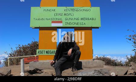 Magelang, Indonesia - 06 08 2019: L'espressione di un uomo seduto sotto il segno di un picco di Merbabu che guarda il vasto mare di nuvole Foto Stock