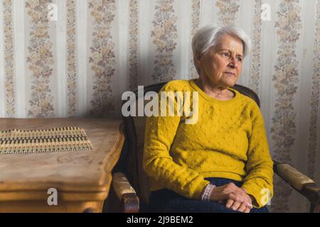 donna anziana di buon-osservare seduta sulla sedia e ponderante circa i problemi medio colpo concetto di anzianità di soggiorno. Foto di alta qualità Foto Stock